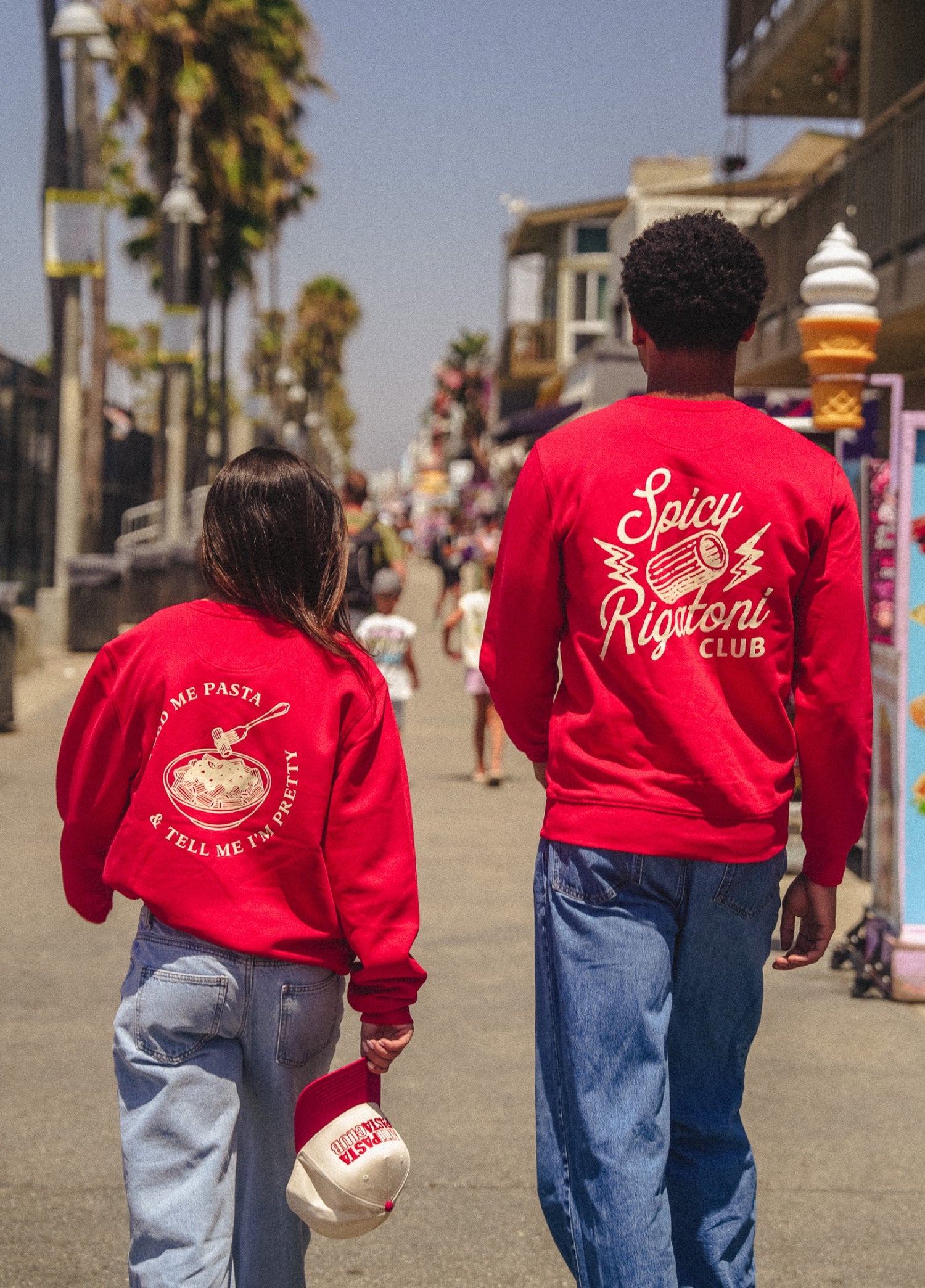 Two models in red MMH crewnecks walking the Venice boardwalk